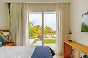 A hotel room with a bed, a desk, a TV, and a balcony with a view of greenery.