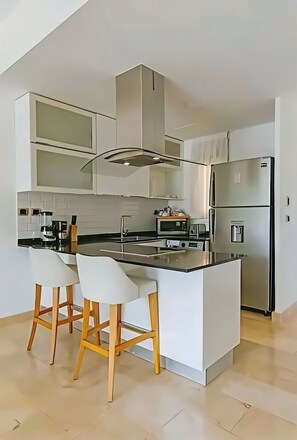 A modern kitchen with a central island, bar stools, and stainless steel appliances.