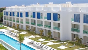 Een modern hotel met een zwembadgedeelte, meerdere balkons en een verzorgd gazon.