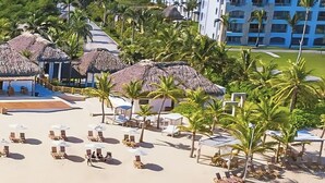 A beach resort with thatched-roof structures, palm trees, and sun loungers. - Ground-floor Apartment (Punta Cana)