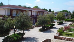 A residential building with a tiled roof, multiple balconies, and a well-maintained garden with trees and shrubs. - Peaceful House With Pool and Terrace (Caorle)