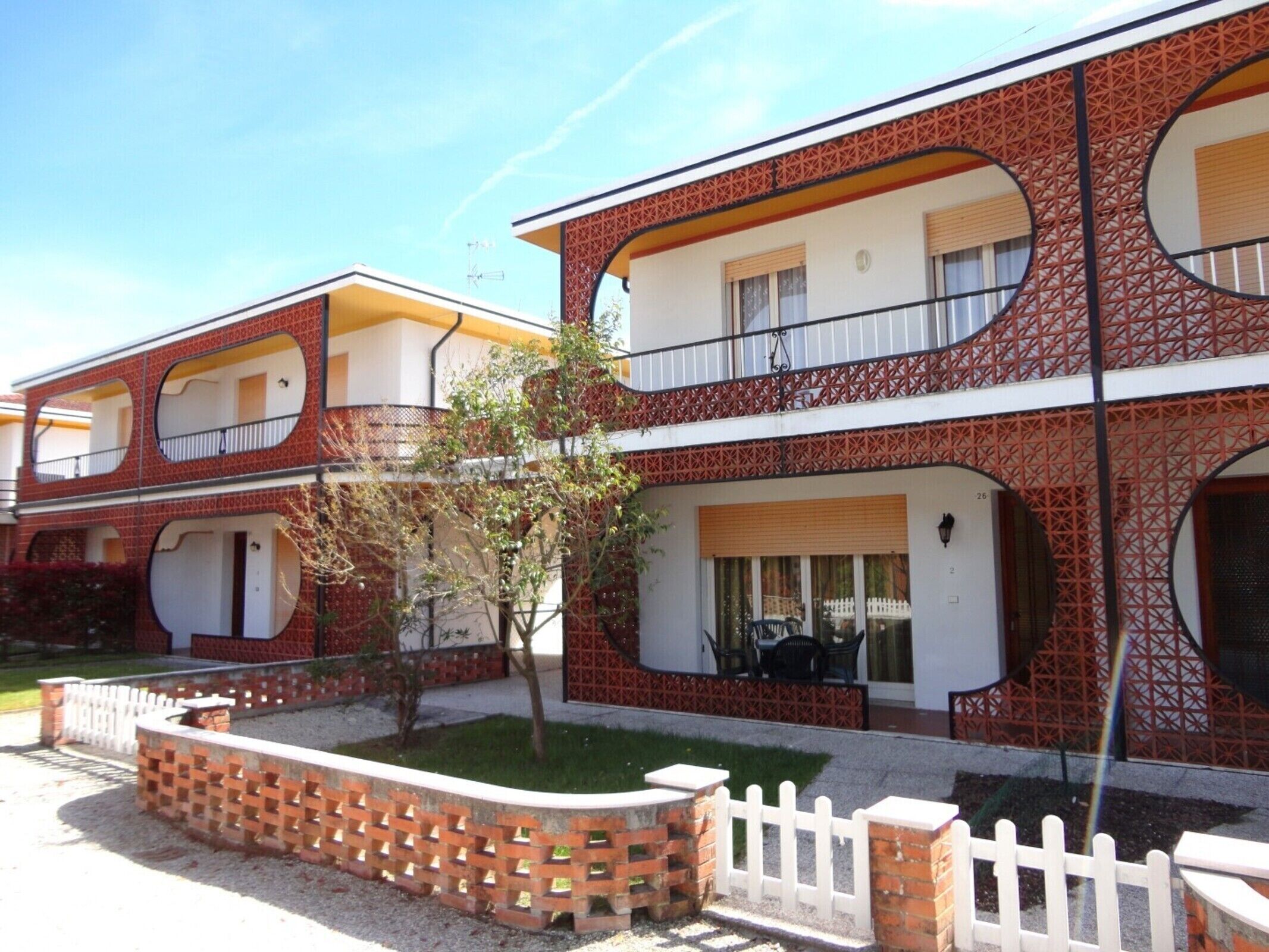 A two-story building with a brick facade, multiple balconies, and a small garden area.