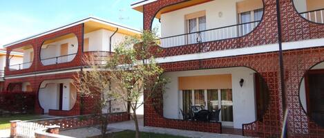 A two-story building with a brick facade, multiple balconies, and a small garden area.