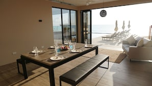 A dining area with a table set for four, a bench, and a view of the ocean. - Room-villa Bluu at the Beach (Jambiani)