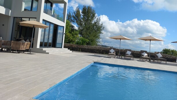 A modern building with a pool, outdoor seating, and a stone wall. - Room-villa Bluu at the Beach (Jambiani)