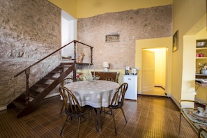 Cozy dining area with a round table and wooden chairs, featuring a stone wall and a staircase leading to an upper level.