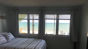Ein Schlafzimmer mit einem Bett, zwei Fenstern mit Meerblick, Holzboden und einem Nachttisch.