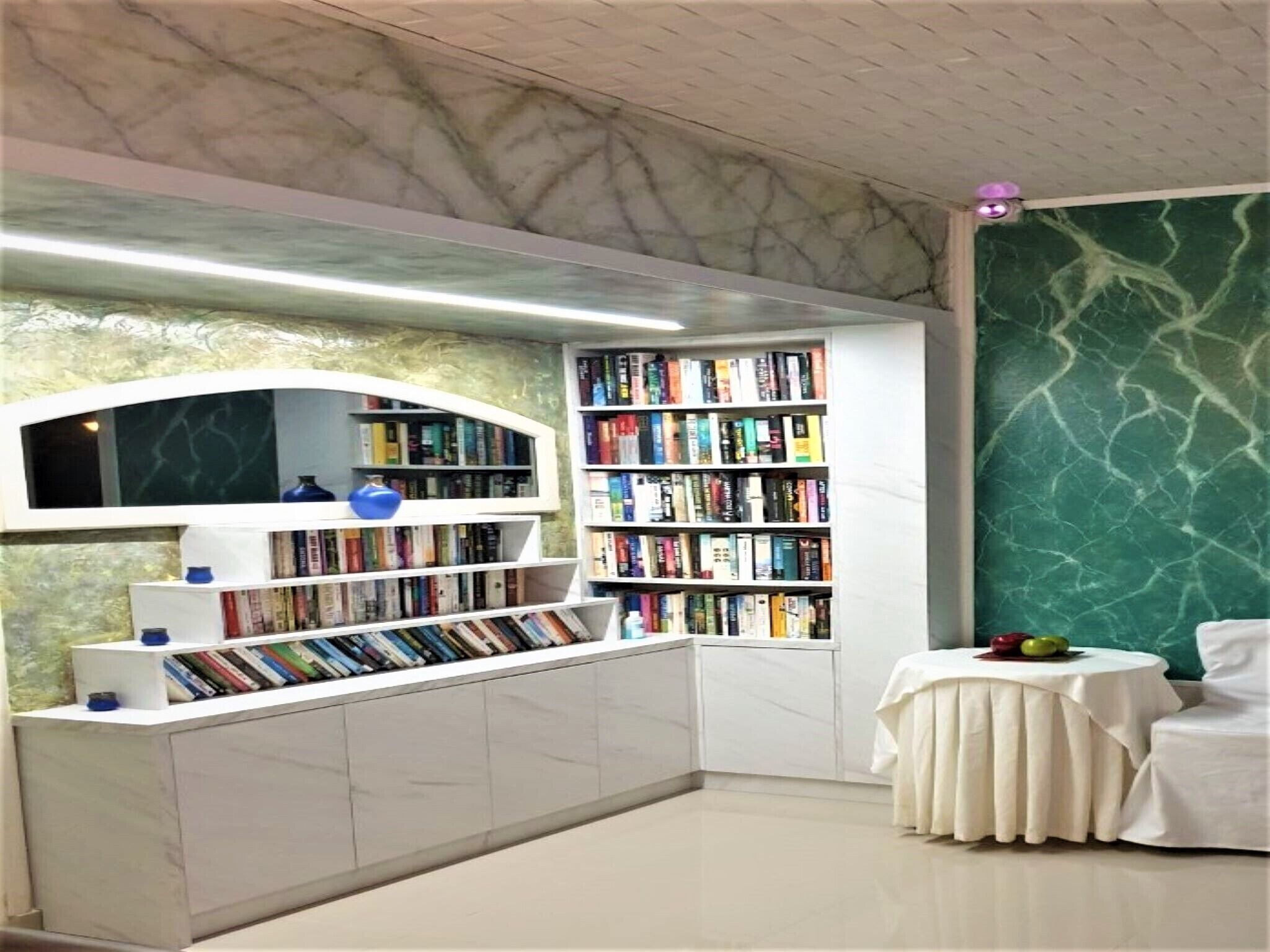 Une bibliothèque moderne avec des murs en marbre, une étagère blanche et une petite table sur laquelle se trouve un panier de fruits.