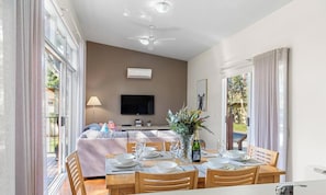 A dining area with a table set for four, a flat-screen TV mounted on the wall, and an air conditioning unit above it.