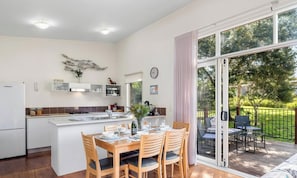 A modern kitchen with a central island, dining area with wooden chairs, and a sliding glass door leading to an outdoor deck.