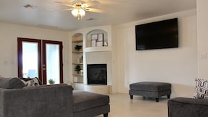 Una sala de estar con chimenea, un televisor de pantalla plana y un ventilador de techo.