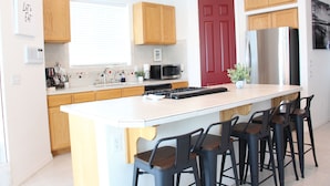 Una cocina moderna con armarios de madera, un refrigerador de acero inoxidable, un microondas y una isla grande con taburetes de bar.