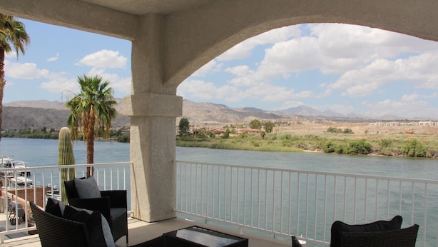 Un balcón con muebles de mimbre, con vistas a un río y montañas al fondo.