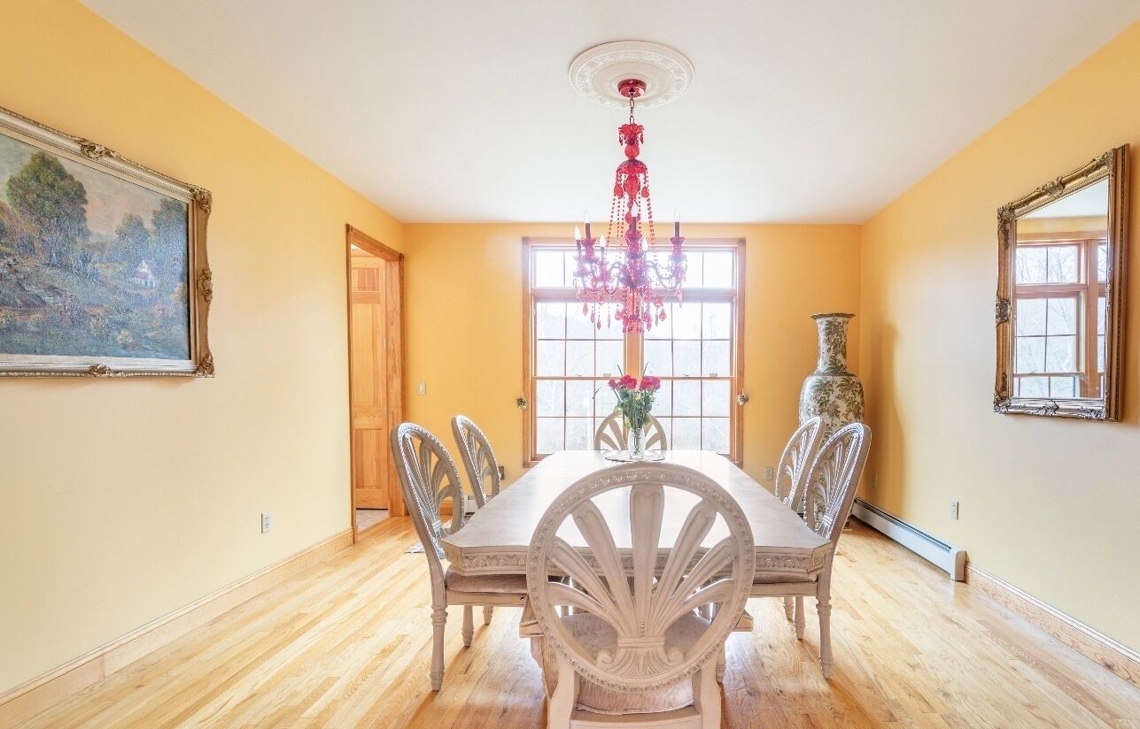 A dining room with a wooden table, chairs, a chandelier, and a vase with flowers.