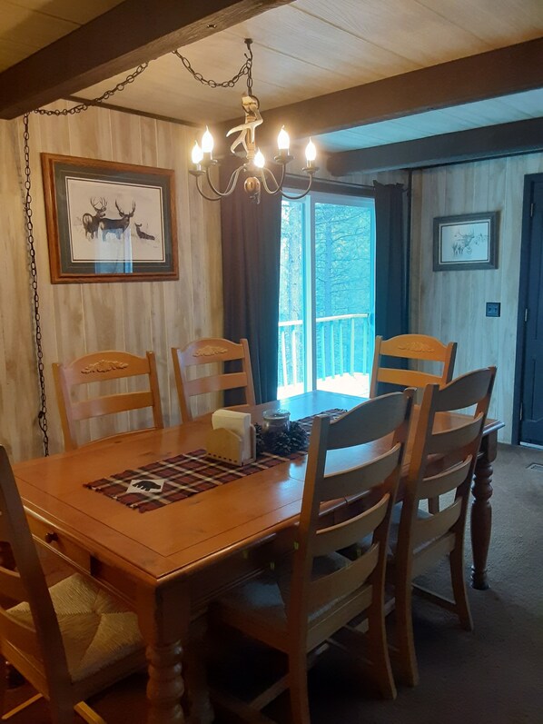 A dining area with a wooden table, four chairs, a chandelier, and framed deer pictures on the walls.