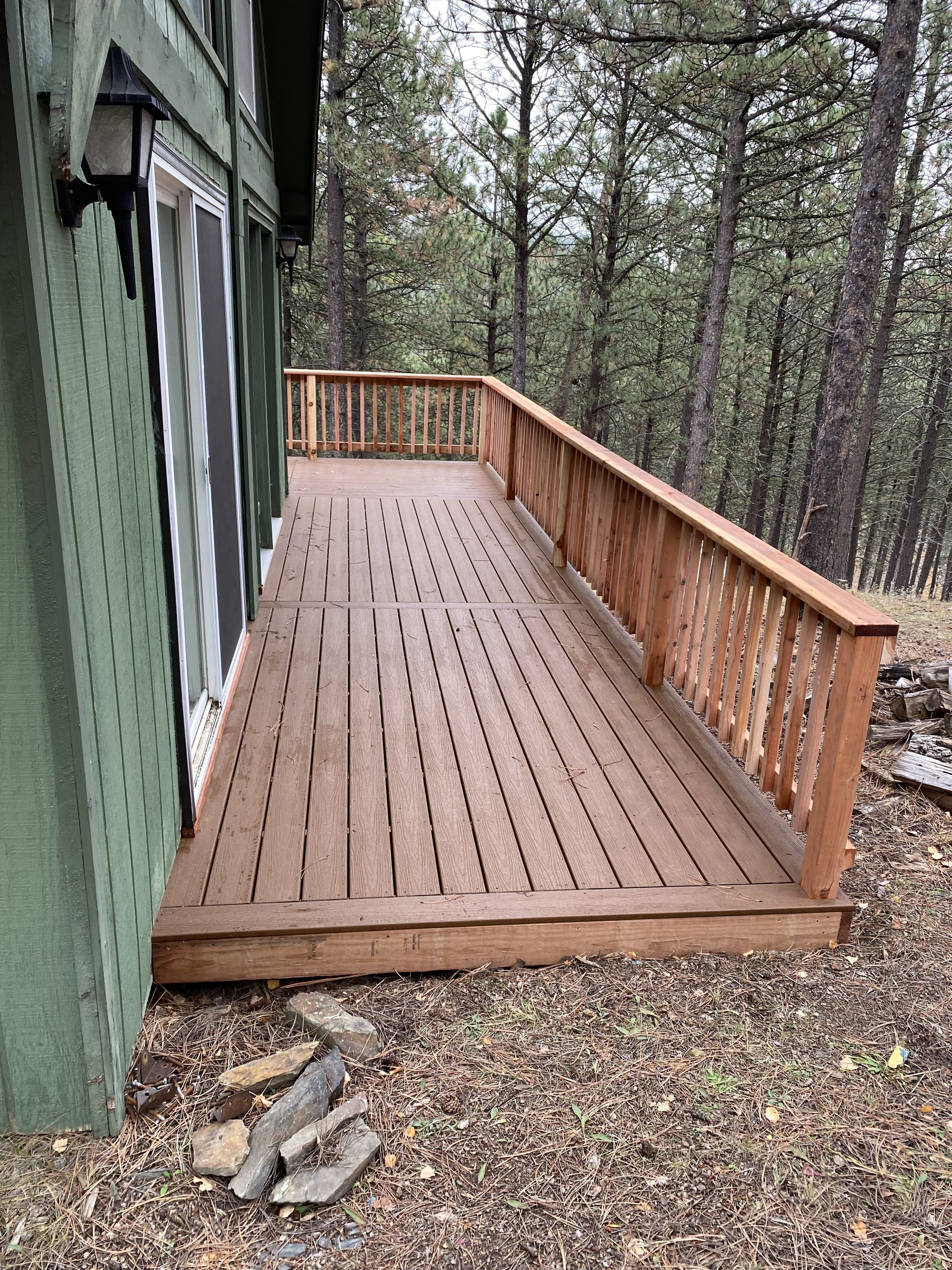 A wooden deck with a railing, surrounded by trees.