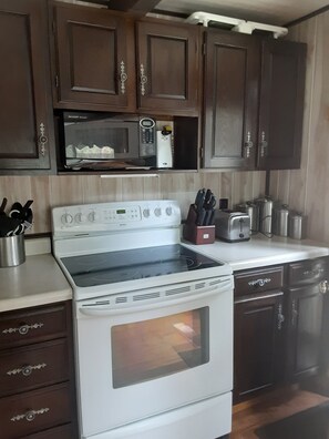 A kitchen with a white stove, a microwave, and dark wooden cabinets. - Cabin in Pines Near Pactola Lake, ATV Trails, Mt. Rushmore, Wi-Fi & Deck! (Rapid City)
