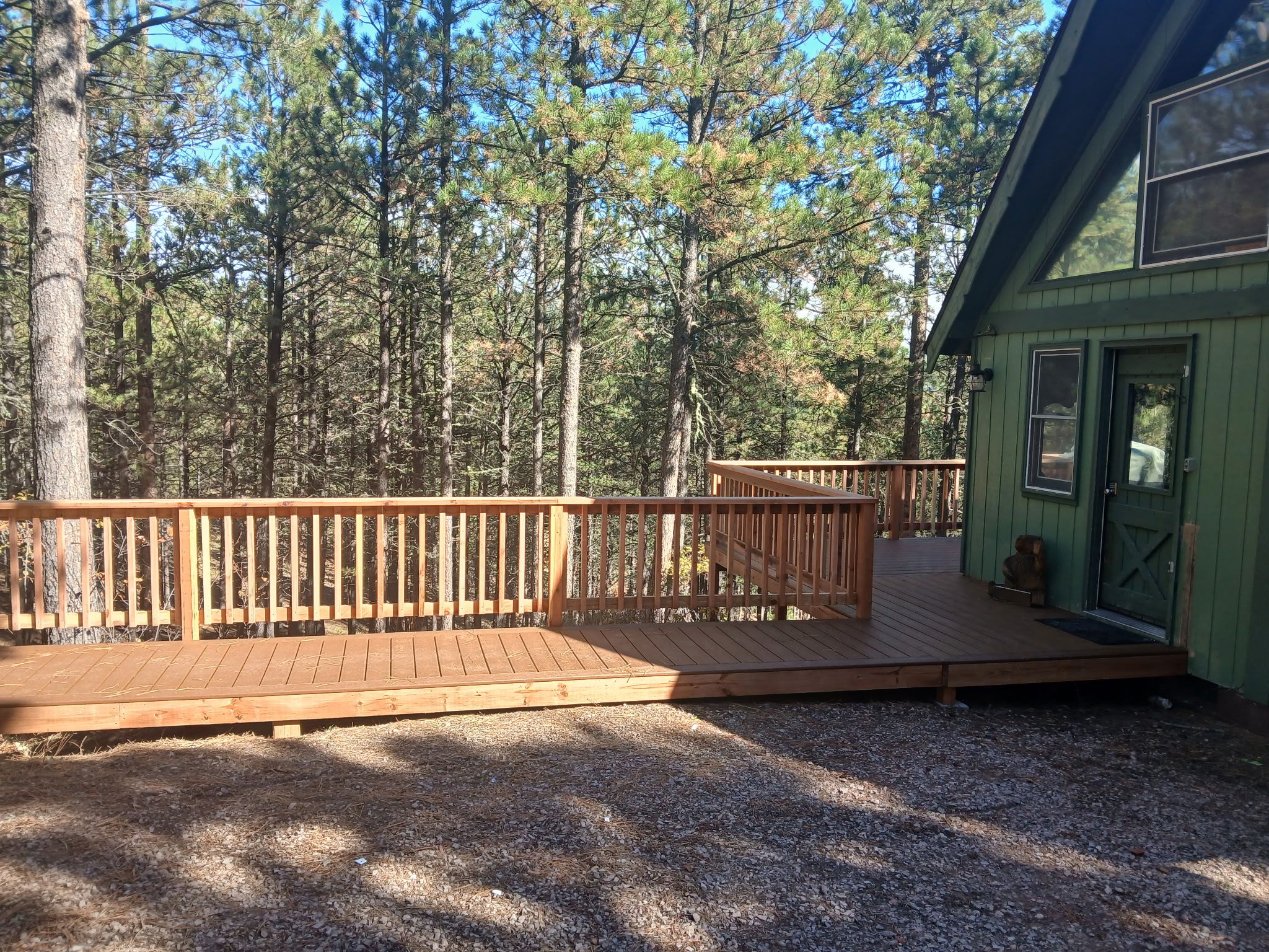 A wooden deck with a railing, leading to a building with a green door and windows.