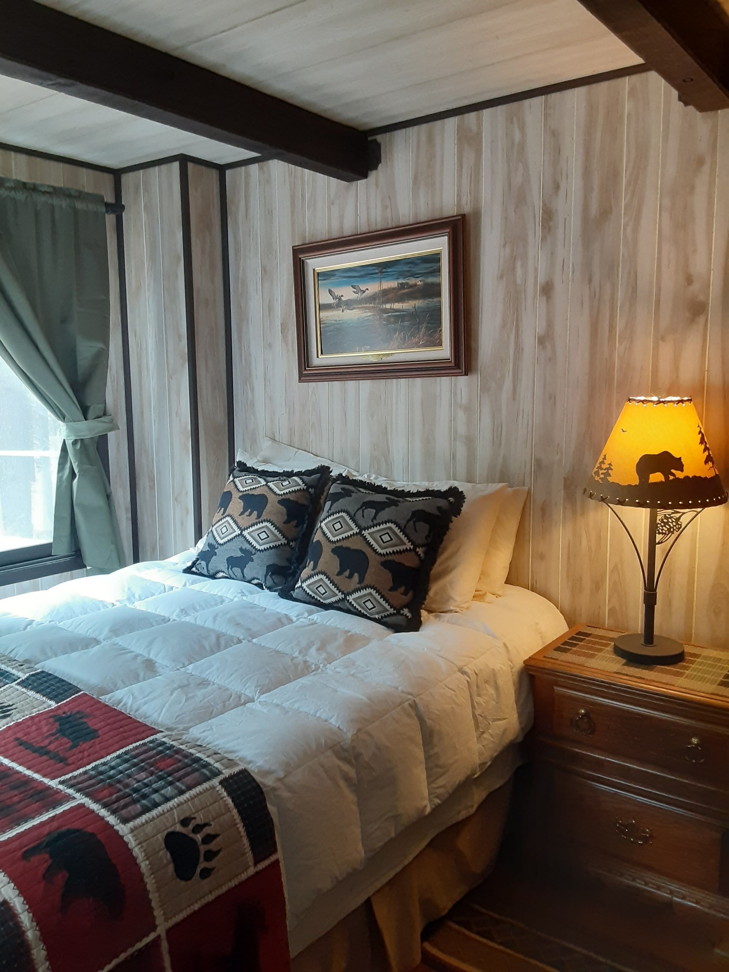A bedroom with a bed, pillows, a nightstand, a lamp, and a painting on the wall.