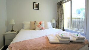 A neatly made bed with a pink blanket, two bedside lamps, and a window with curtains. - Fermoy Cottage (Yarra Ranges)
