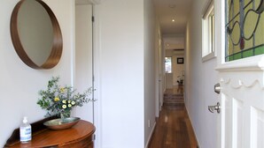 A hallway with wooden flooring, a round mirror on the left, a door at the end, and a window with stained glass on the right. - Fermoy Cottage (Yarra Ranges)