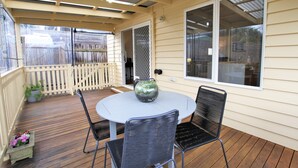 A covered patio with a round table and two chairs, a potted plant, and a wooden fence. - Fermoy Cottage (Yarra Ranges)