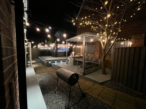 Un espacio de patio al aire libre con una parrilla, asientos e iluminación colgante.