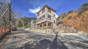 A multi-story building with a stone facade and a balcony, located in a hilly area with a clear sky.