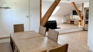 Un comedor con una mesa y sillas de madera, un sofá negro y una cocina al fondo.