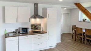 Una cocina moderna con armarios blancos, una campana extractora de acero inoxidable y una mesa de comedor de madera con sillas.