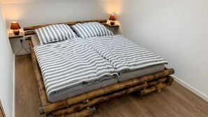Una cama con estructura de bambú, ropa de cama a rayas grises y blancas, y dos lámparas de noche.