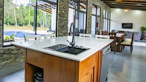 Une cuisine moderne dotée d’un grand îlot central, de murs en pierre et de poutres en bois au plafond.