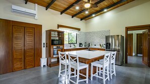 Une cuisine moderne avec des meubles en bois, un îlot central doté de chaises, un four encastré et un réfrigérateur.