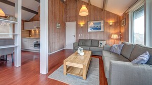 Un salon moderne avec un mur d’accent en bois, un canapé gris, une table basse en bois et une vue sur la cuisine.