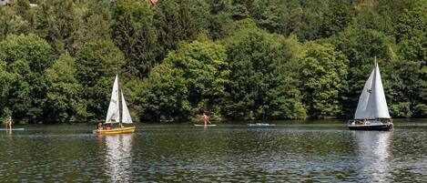 A lake with sailboats and a forested hillside in the background.