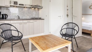 Una cocina compacta con armarios blancos, una estufa y una cafetera. Hay dos sillas negras y una mesa de madera.