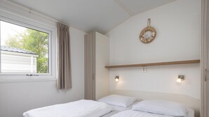 Una habitación con dos camas, una ventana con cortinas, una lámpara fijada en la pared y un adorno decorativo.