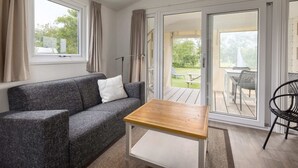Una habitación acogedora con un sofá gris, una pequeña mesa de madera y vistas a un patio exterior con mesa y sillas.