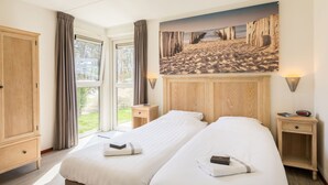 Hotelkamer met twee bedden, een houten garderobe, een schilderij van een strand en uitzicht op het omliggende landschap.