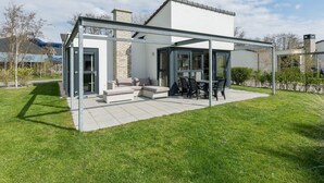 Een modern huis met een glazen patio, zitplaatsen buiten en uitzicht op het omliggende landschap.