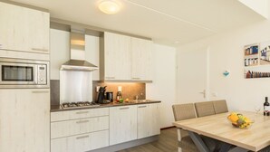 Een moderne keuken met witte kasten, een gasfornuis, een magnetron en een eethoek met een tafel en stoelen.