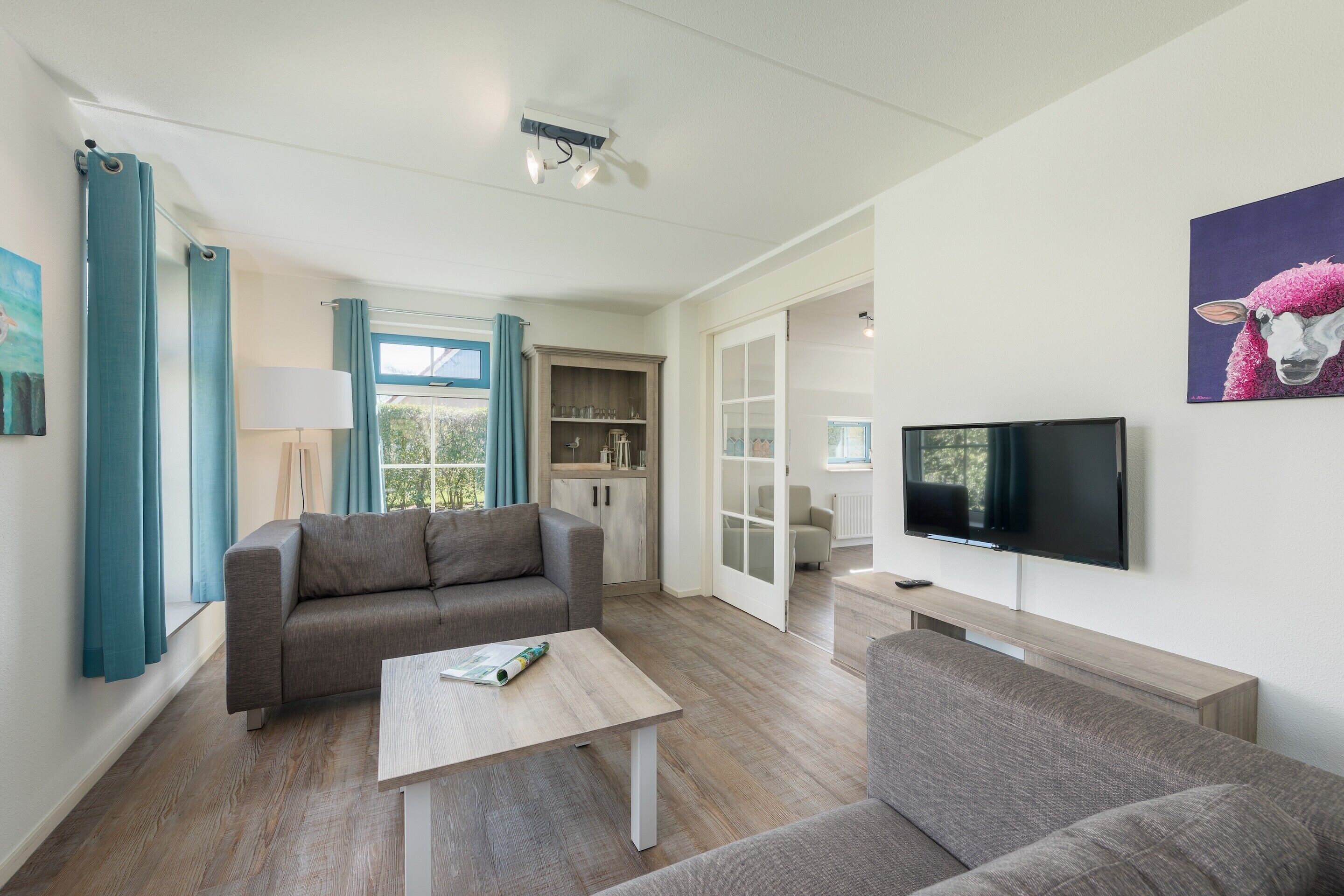 Una sala de estar moderna con un sofá gris, una mesa de centro y un televisor sobre un soporte de madera.