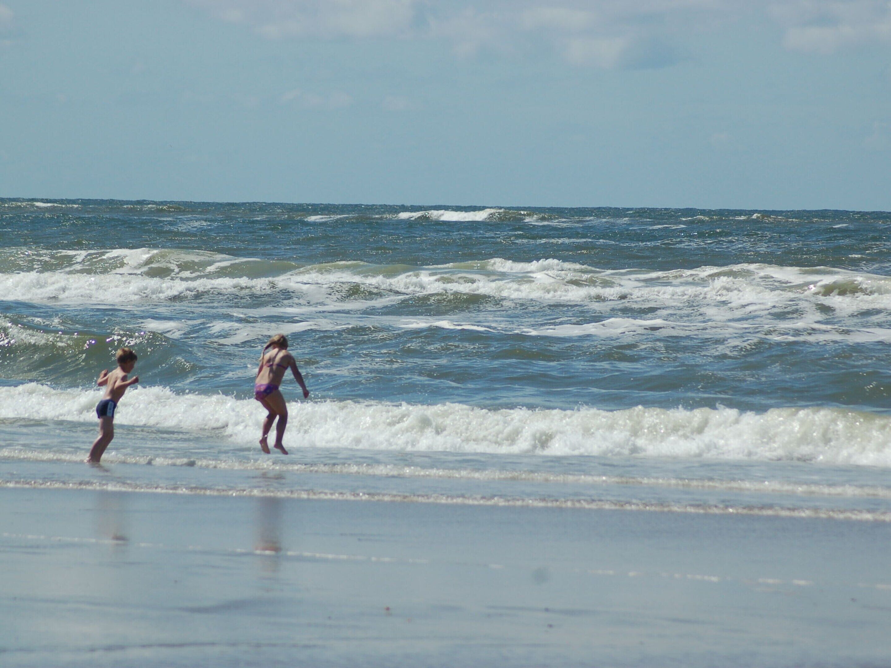 Una playa con olas y dos personas en traje de baño.