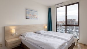 Quarto de hotel com duas camas, um quadro na parede e vista para barcos através de uma grande janela.
