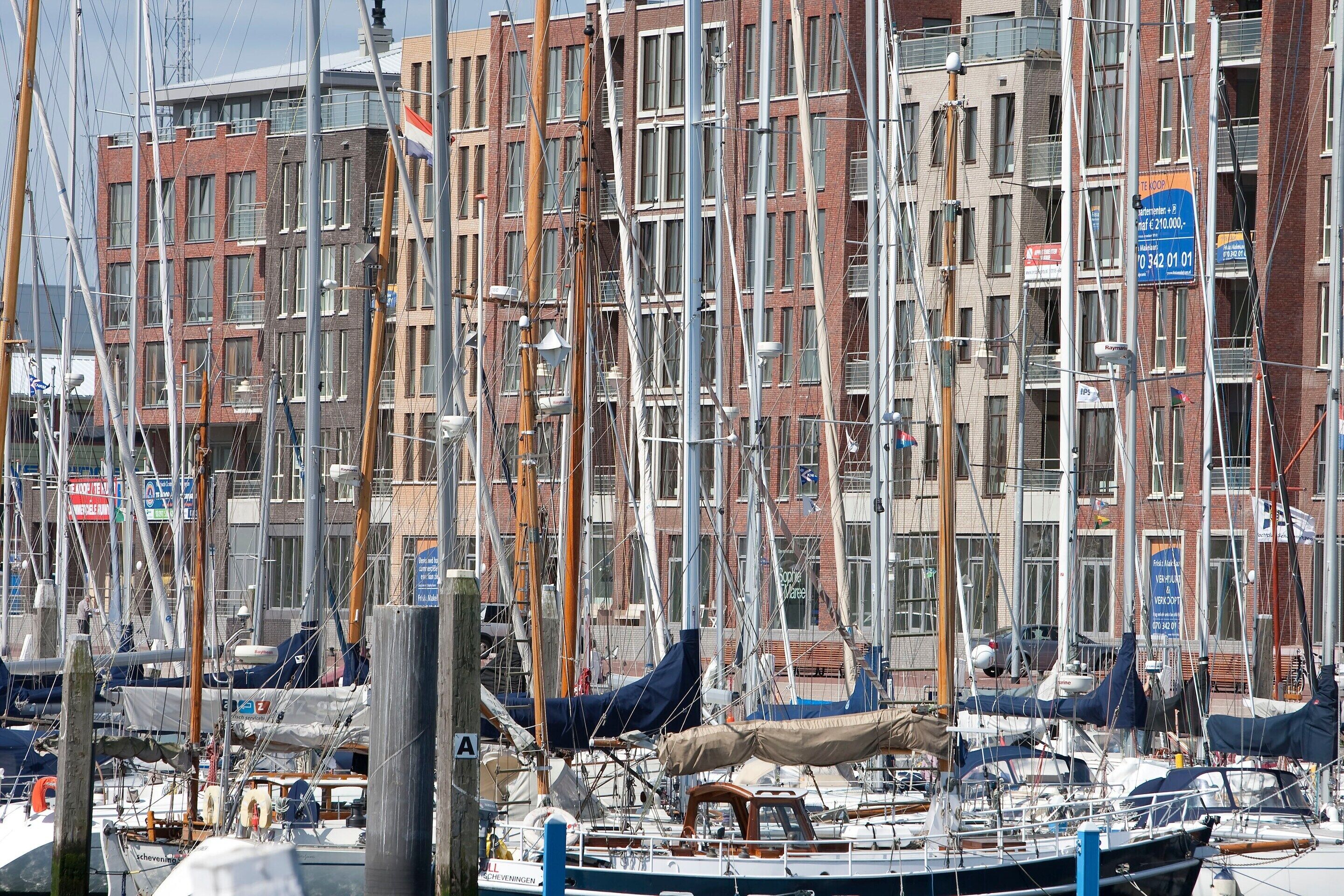 Un port de plaisance où sont amarrés de nombreux bateaux, entouré d’immeubles à plusieurs étages dotés de balcons et de fenêtres apparents.