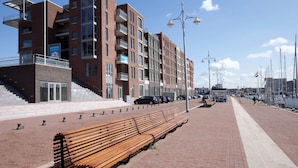 Un moderno edificio de apartamentos con fachada de ladrillo, balcones y un banco de madera a lo largo del paseo marítimo.