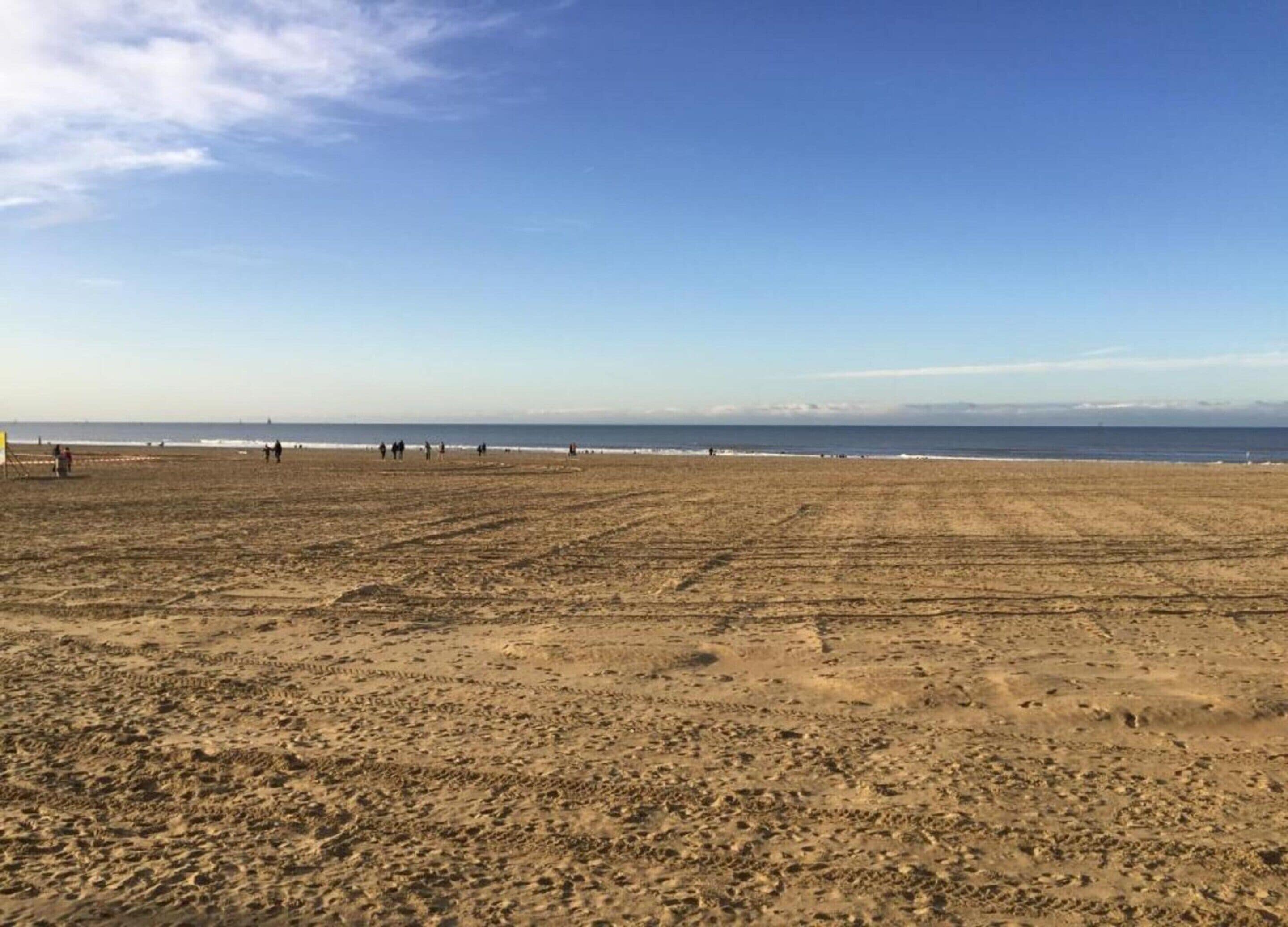 A wide, open sandy beach with a clear sky and calm sea.