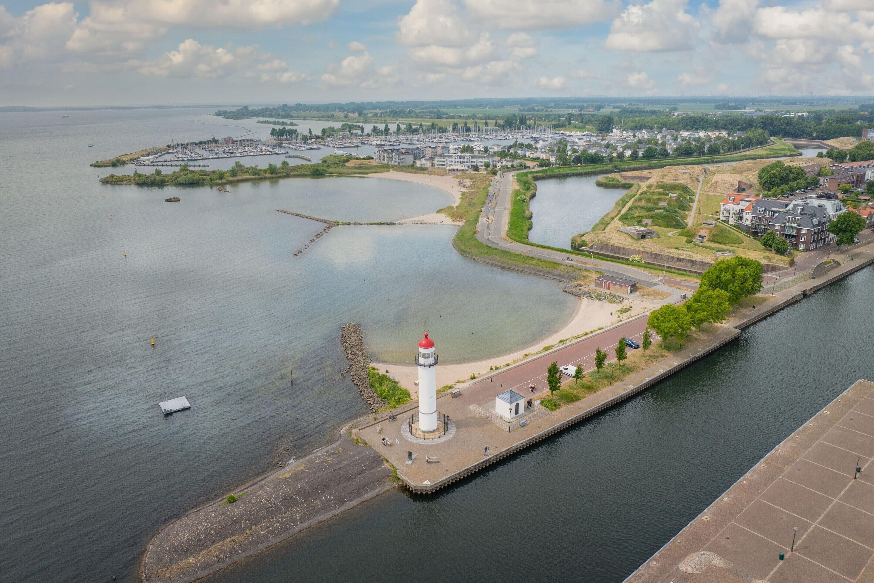 Una zona frente al agua con un faro, un puerto deportivo y un río.