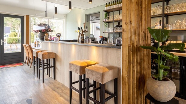 Un espace bar avec des tabourets en bois, un comptoir et des étagères remplies de bouteilles et de verres.