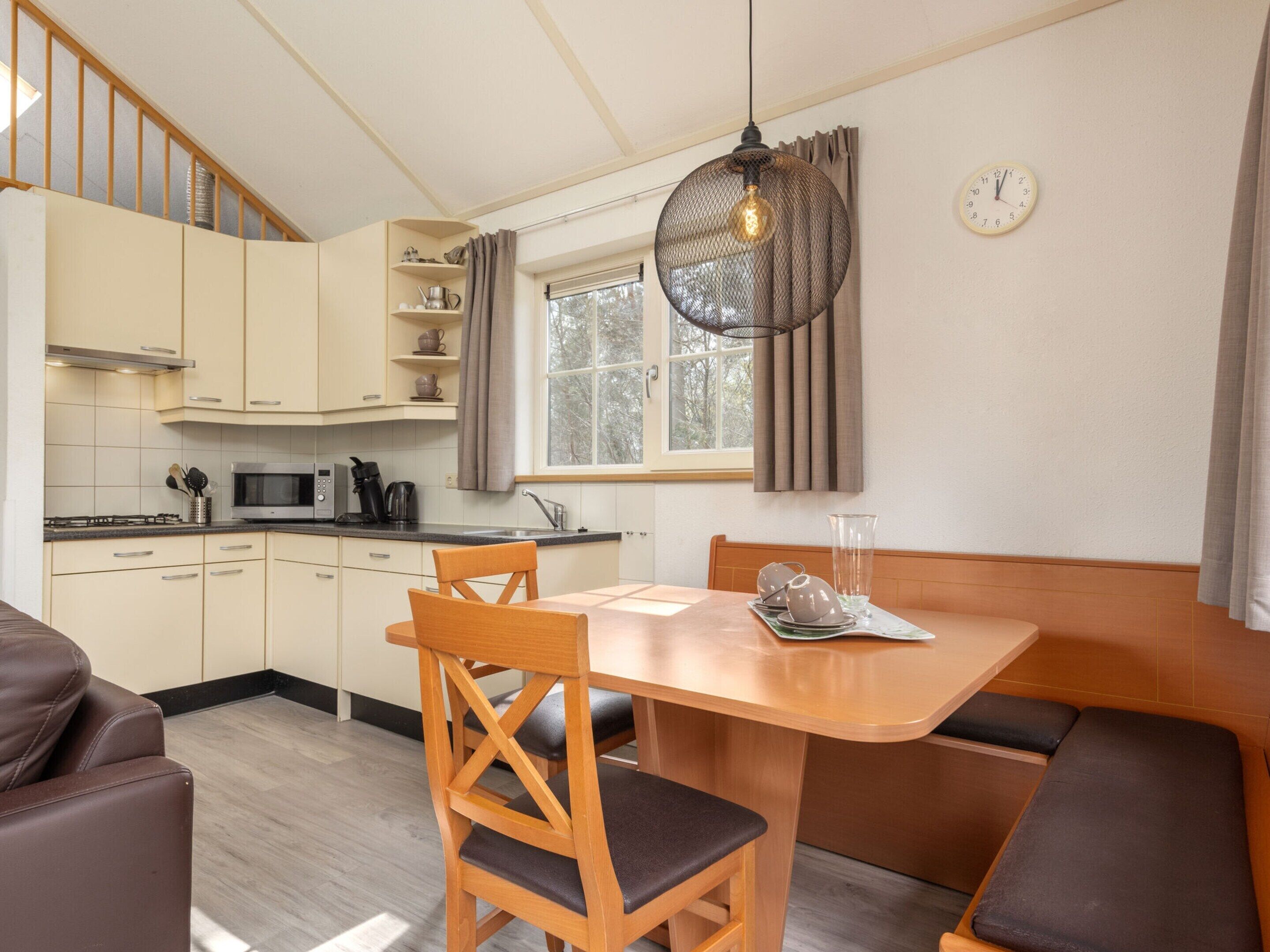 Una cocina compacta con comedor, muebles de madera y una lámpara colgante.